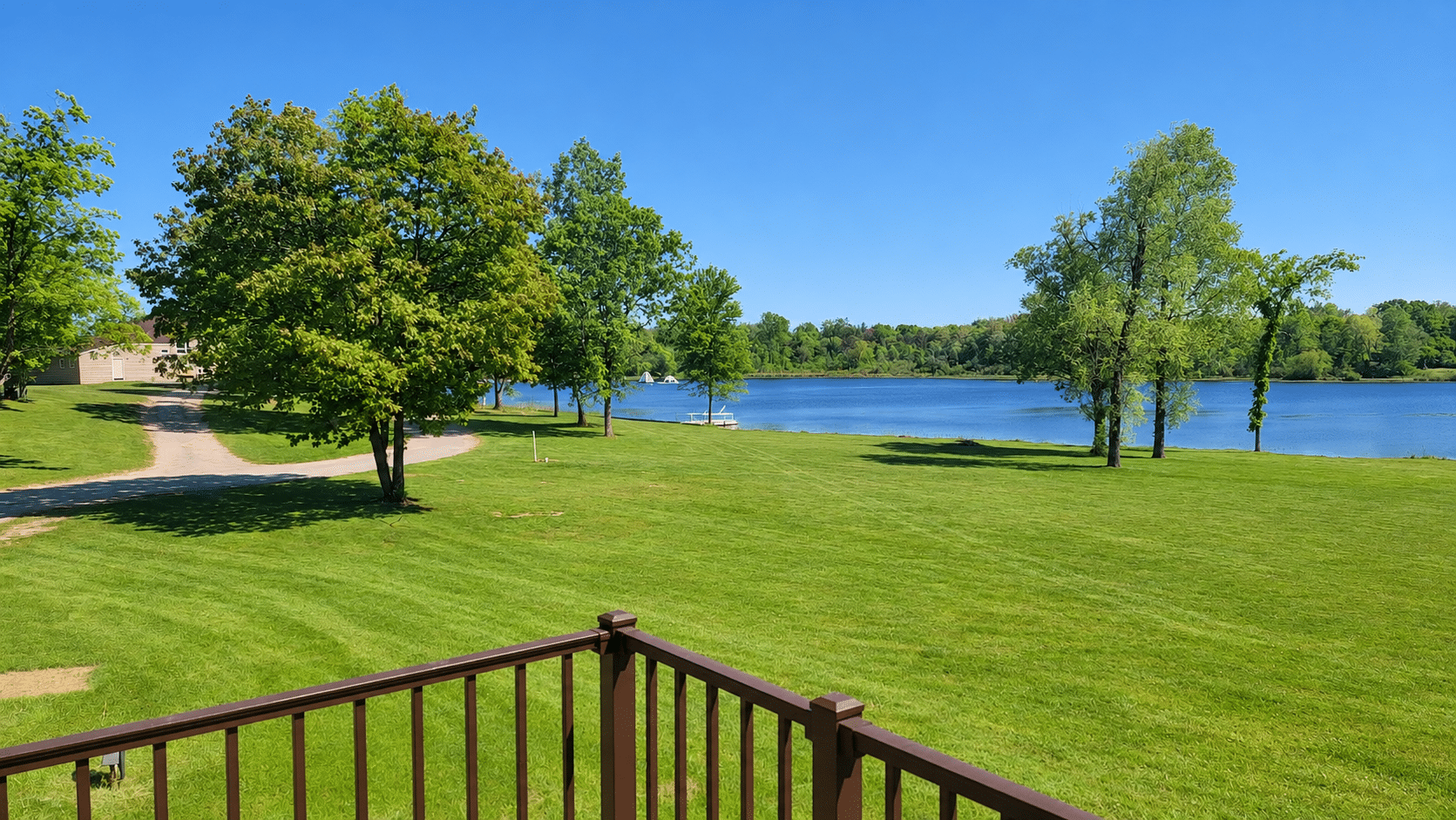 View from the wooden deck across OLF’s green lawn toward the lake under a bright blue sky.